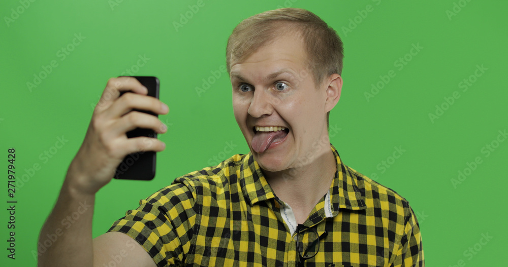 Caucasian young man in yellow shirt taking funny selfies on the smartphone Caucasian young man in yellow shirt taking funny selfies on the smartphone
