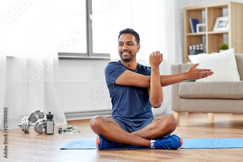 sport, fitness and healthy lifestyle concept - indian man training and stretching arm at home photo