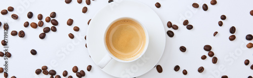 panoramic shot of delicious coffee in cup near scattered roasted beans on white background
