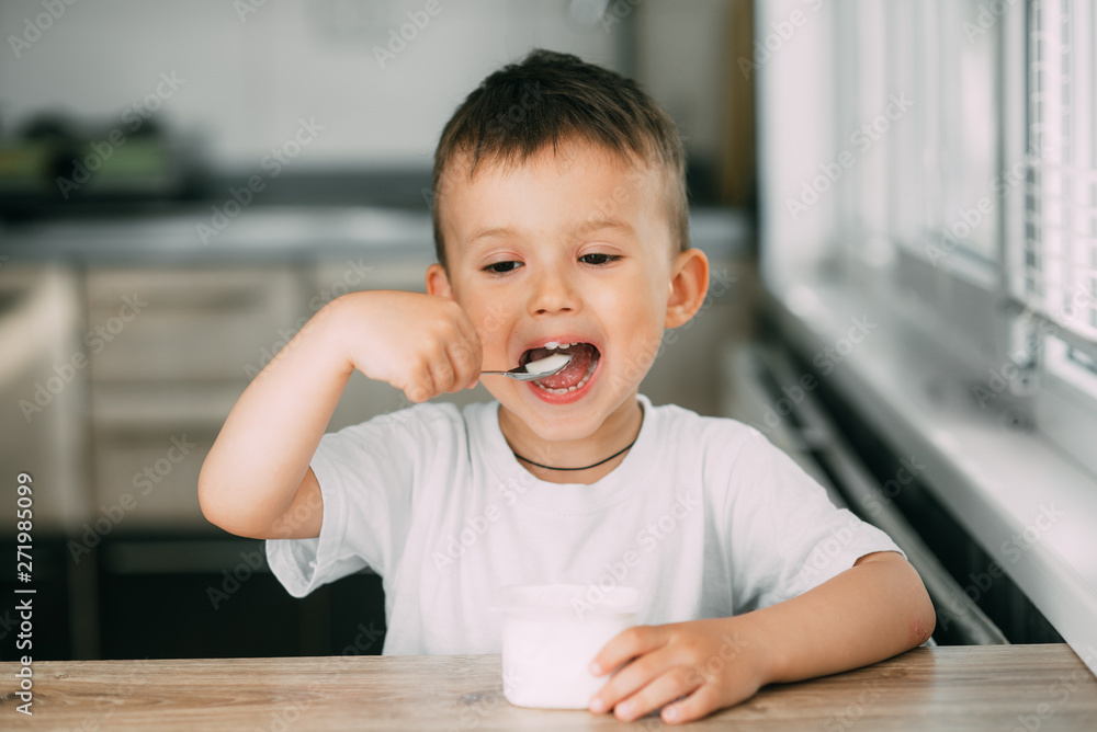 Adorable little boy eating yogurt in the kitchen in the afternoon Adorable little boy eating yogurt in the kitchen in the afternoon
