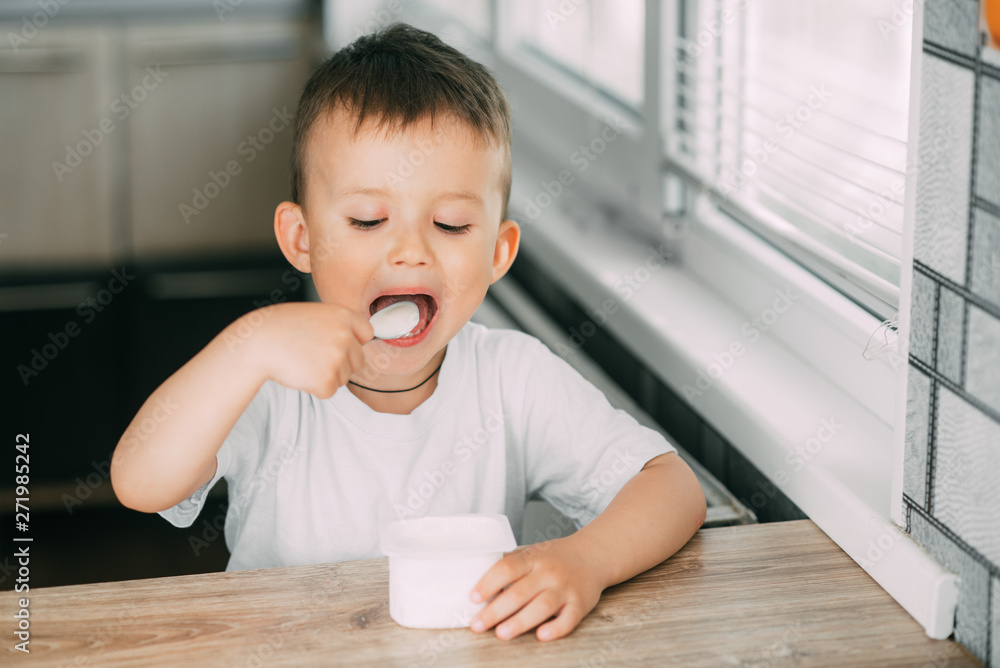 Adorable little boy eating yogurt in the kitchen in the afternoon Adorable little boy eating yogurt in the kitchen in the afternoon