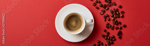 top view of delicious coffee in cup near roasted beans on red background, panoramic shot