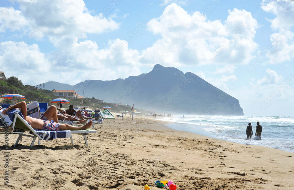 Relaxed people on the Sabaudia beach for the summer holidays. The Circeo Mountain on the background. Sabaudia, Lazio, Italy. Relaxed people on the Sabaudia beach for the summer holidays. The Circeo Mountain on the background. Sabaudia, Lazio, Italy.