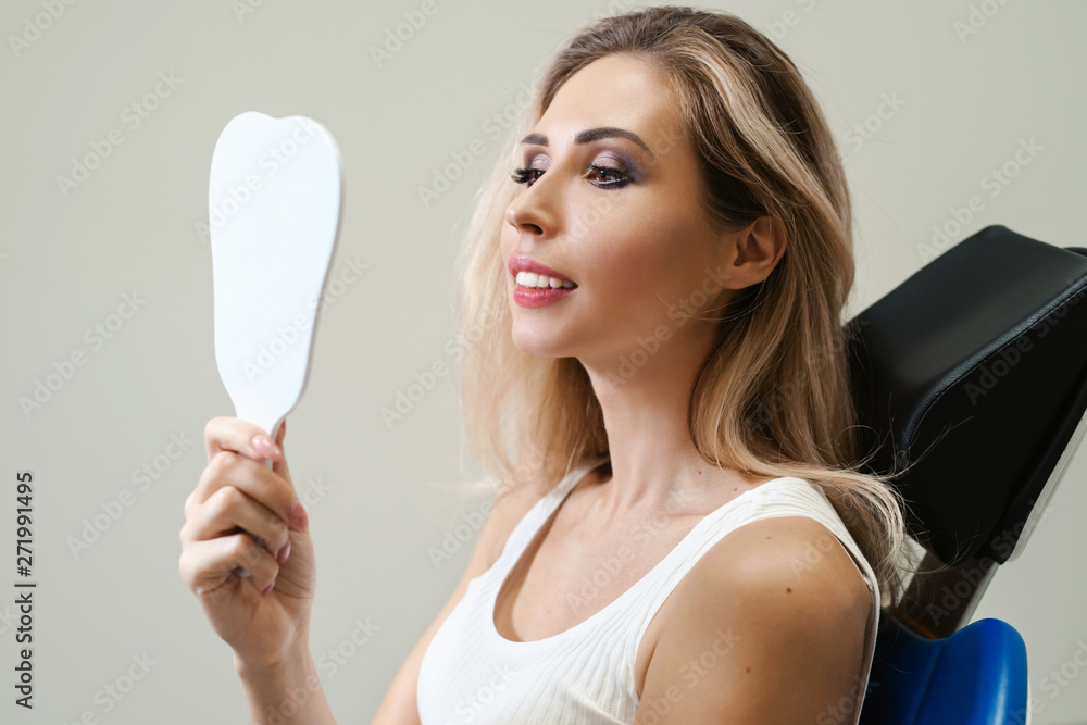 Young woman patient checking teeth in mirror in dentistry. Female at the dentist office. Young woman patient checking teeth in mirror in dentistry. Female at the dentist office.