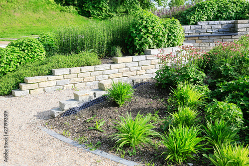 Moderner Garten- und Landschaftsbau: Gehweg und Mauern aus Natursteinen mit integrierten Sitzbänken und Anpflanzungen 