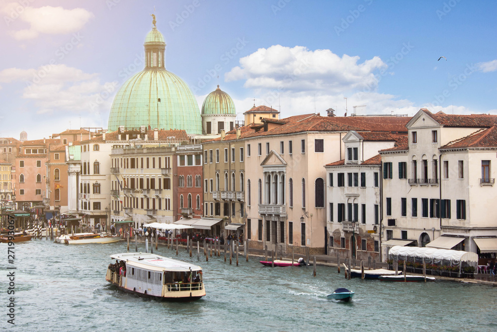 The cityscape view of Venice the Grand Canal with touristic and cruise boats. Sunny bright day and blue sky above the facades of ancient buildings in Italian architectural style. Summet vacation.