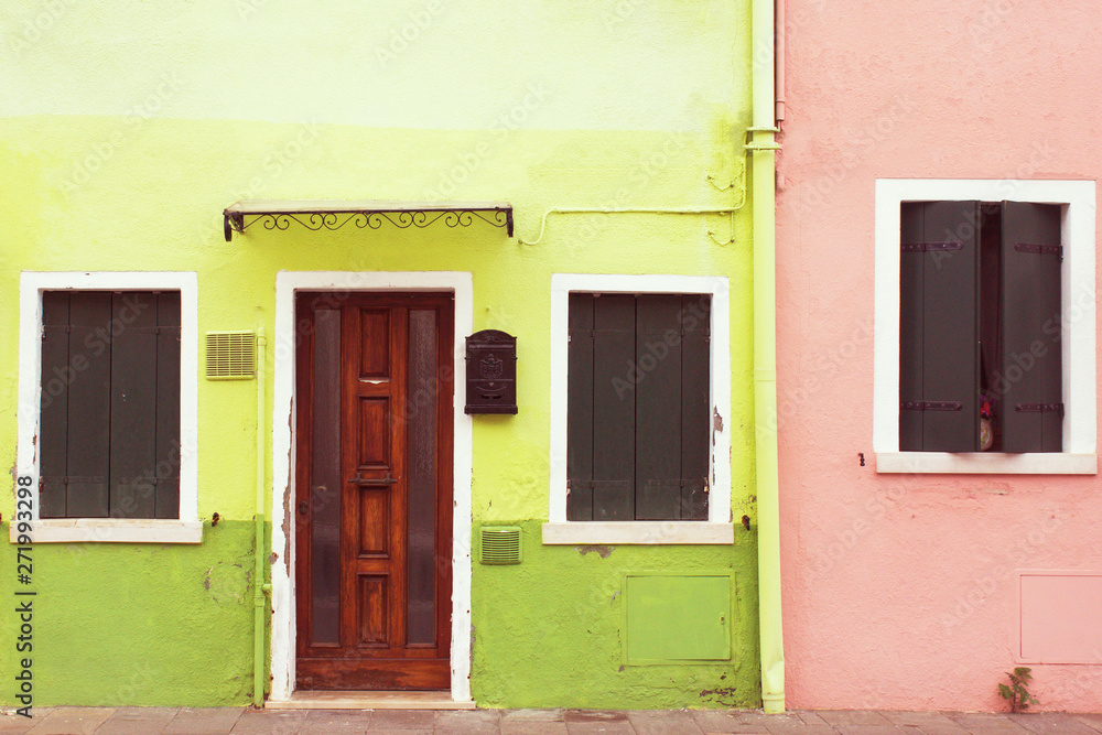 Bright green, lime and pink color painted facades of residential buildings. Old wooden entrance door and closed wooden shutter windows. Traditional colorful architecture.