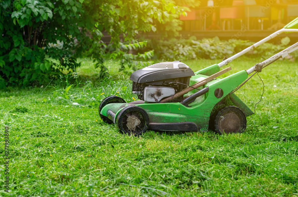 Green gasoline lawn mower on the grass in the park on the lawn Green gasoline lawn mower on the grass in the park on the lawn