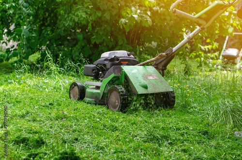 Green gasoline lawn mower on the grass in the park on the lawn