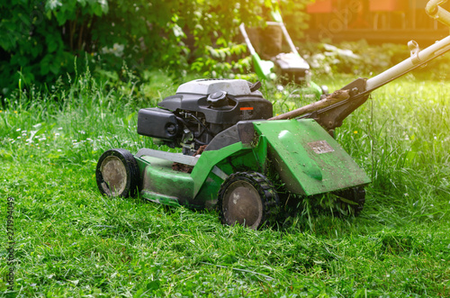 Green gasoline lawn mower on the grass in the park on the lawn