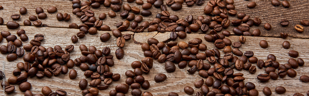 Naklejka premium panoramic shot of wooden rustic table with scattered roasted coffee beans
