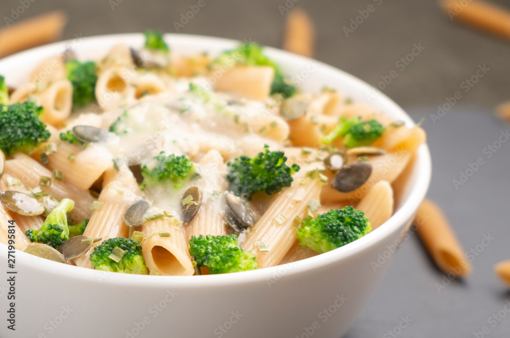 White bowl filled with pasta with broccoli and pumpkin seeds. The dish is poured with white sauce.