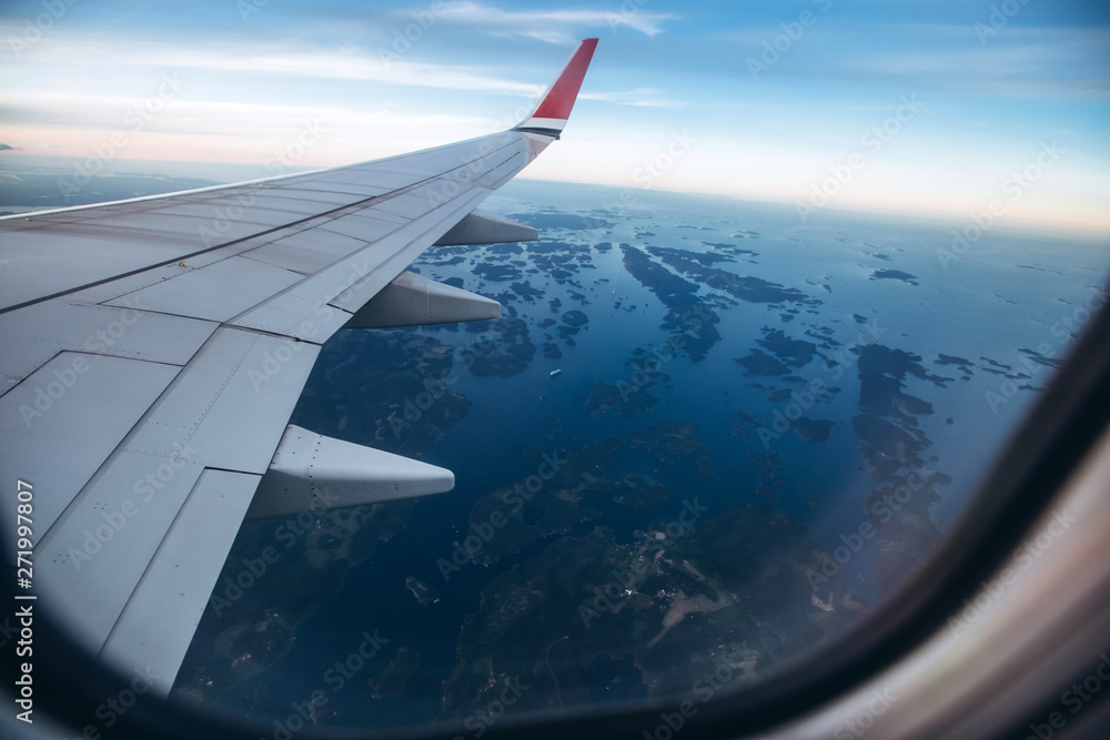Obraz premium aircraft wing in the sunset light. Airplane wing against the blue sky from the porthole. view from the airplane porthole to the clouds.