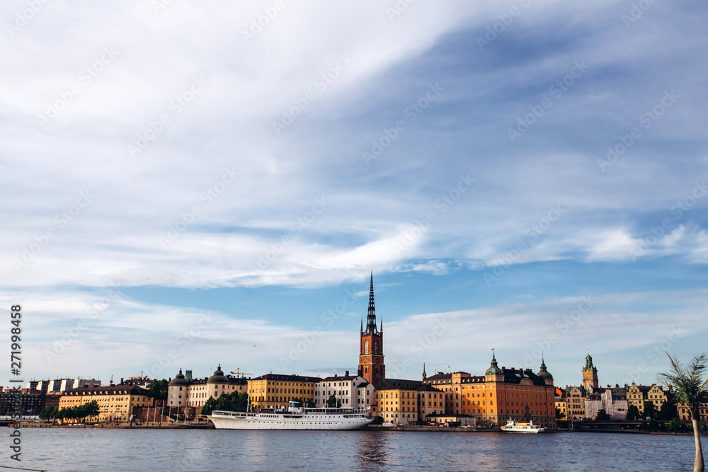 Scenic summer panorama of the Old Town (Gamla Stan) architecture in Stockholm, Sweden. view from Monteliusvagen hill on island Riddarholm and tower of church. Lake Malaren with blue sky, white clouds.