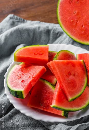 Cut slices of juicy watermelon on white plate on wooden table background