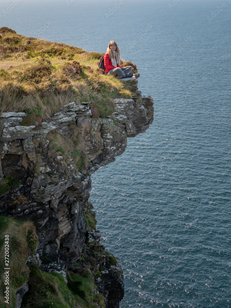 Young woman sitting on the edge of a cliff at the Irish west coast - travel photography