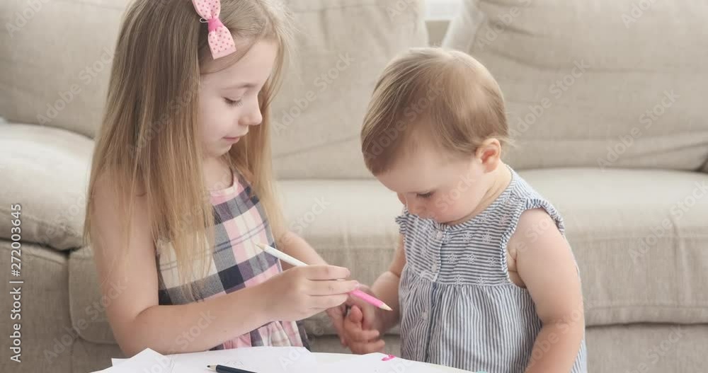 Girl holding hands of her baby sister and teaching her to draw with colored pencil Girl holding hands of her baby sister and teaching her to draw with colored pencil