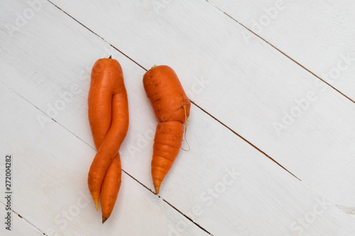 Two ugly carrots on white wooden background. Image with copy space, top view.