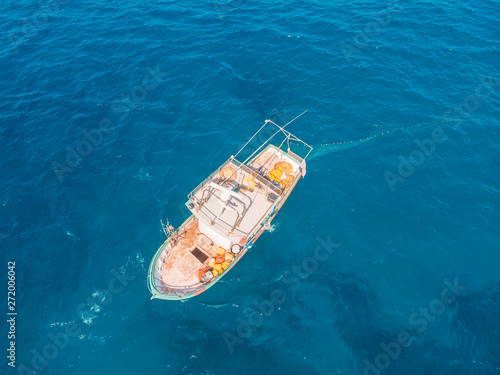 Fishing boat in blue sea water, fishermen set nets for fish. Aerial top view © Parilov