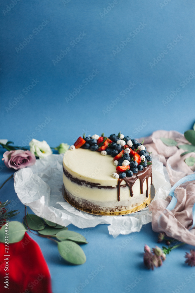 Sweet cake with berries and flowers, on a blue background with ribbons and draperies