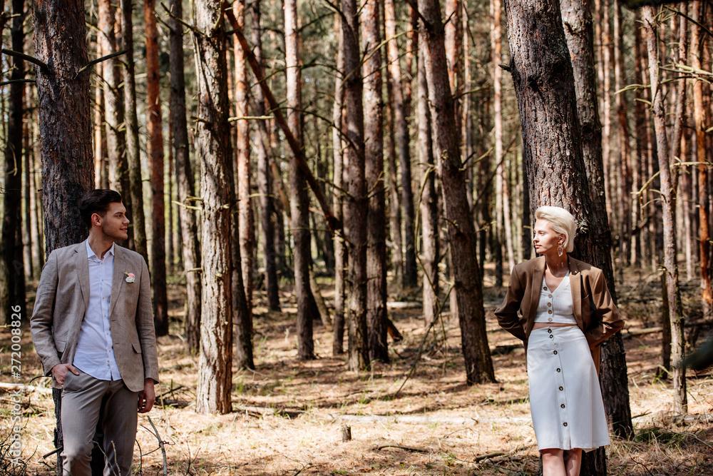stylish bride and bridegroom standing in forest and looking at each other