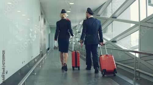 Pilot and stewardess with red suitcases walking by airport. Back view. photo