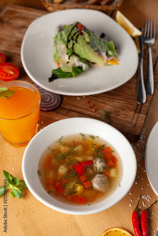 Summer light soup with vegetables and meatballs for the first course and vegan spring rolls for the second course as a part of healthy mid day meal Summer light soup with vegetables and meatballs for the first course and vegan spring rolls for the second course as a part of healthy mid day meal