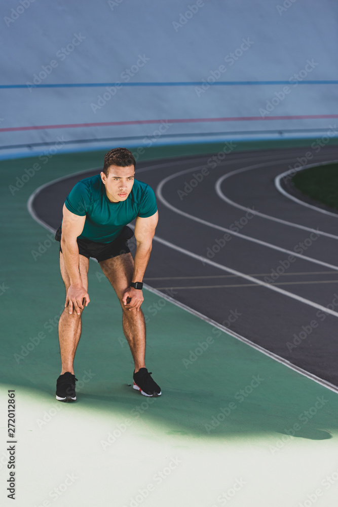 Obraz premium mixed race sportsman with hands on knees standing at stadium