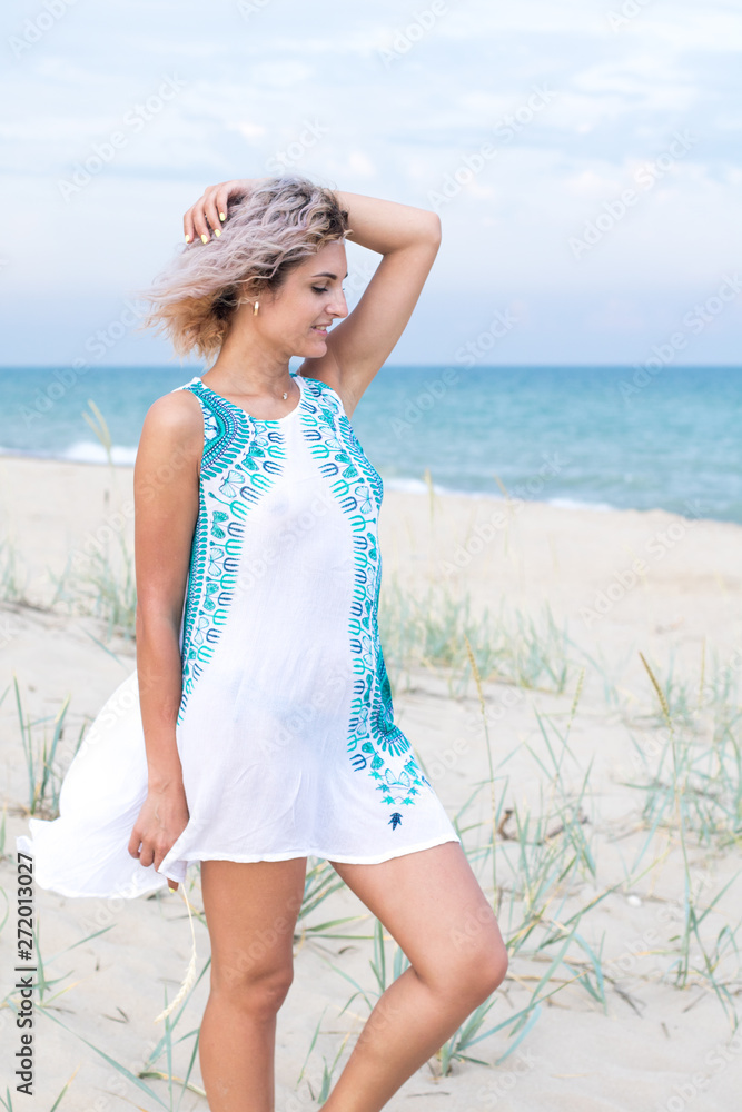 beautiful young woman with curly hairs in white dress with trasery is happy to be on the beach. Ocean and grass on the background beautiful young woman with curly hairs in white dress with trasery is happy to be on the beach. Ocean and grass on the background