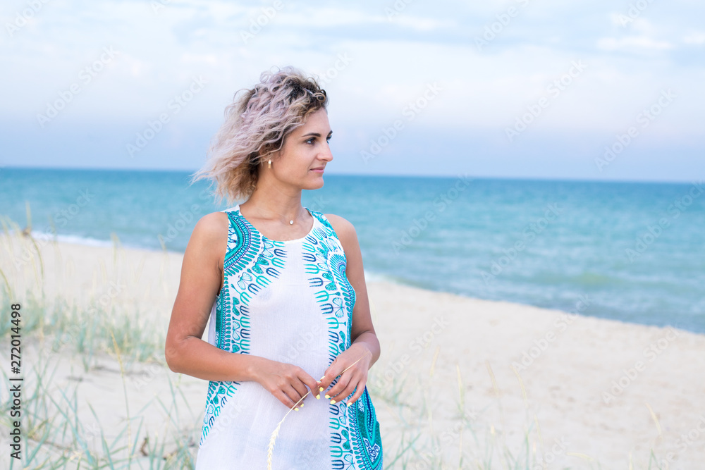 beautiful young woman with curly hairs in white dress with trasery is happy to be on the beach. Ocean and grass on the background beautiful young woman with curly hairs in white dress with trasery is happy to be on the beach. Ocean and grass on the background