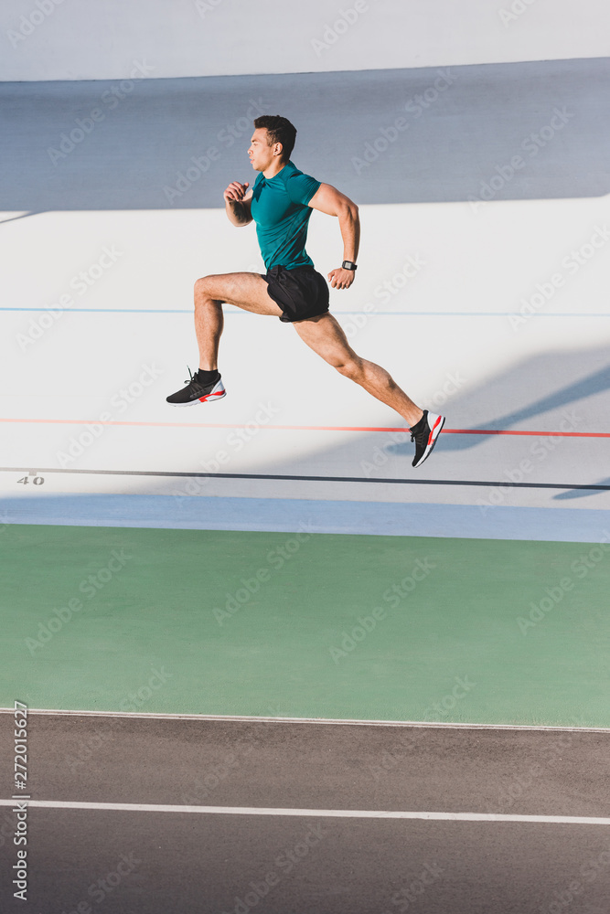 side view of muscular mixed race sportsman sprint running at stadium