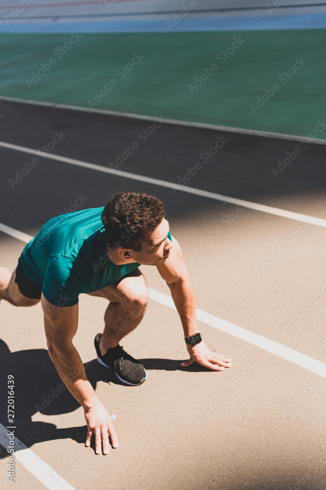 mixed race sportsman on start position on running track, looking away at stadium