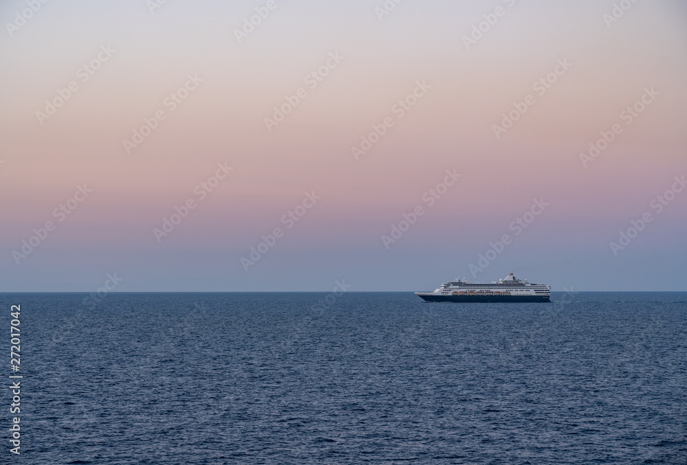Small cruise liner sailing across the ocean as dawn starts to light the sky
