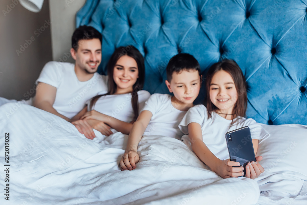 Focus at young, happy family speak with grandmother with kids by phone, lying on bed..Morning relax. Focus at young, happy family speak with grandmother with kids by phone, lying on bed..Morning relax.