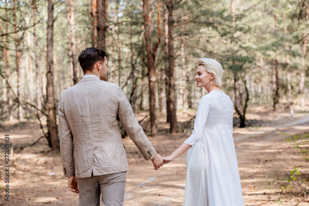 just married couple holding hands and looking at each other in forest