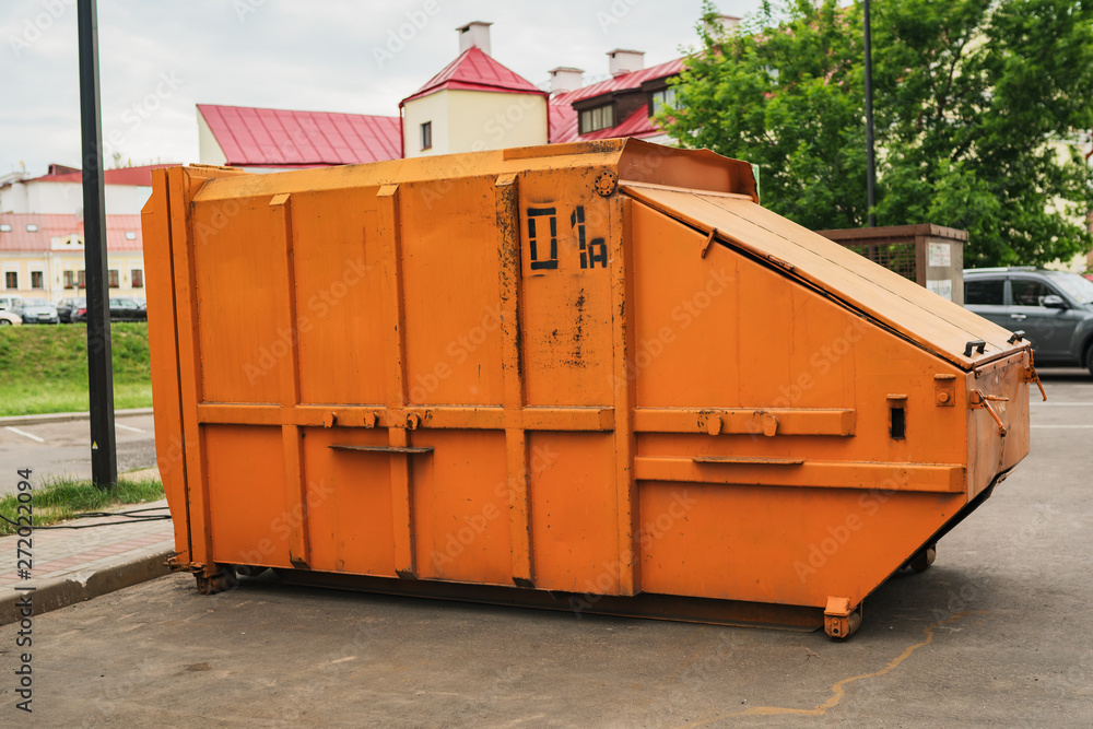 Orange garbage press in the street with sfety signs