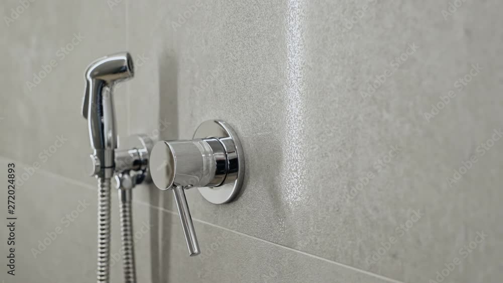 Modern chrome hand shower and mixer fittings mounted on a tiled wall in a bathroom in a close up panning shot Modern chrome hand shower and mixer fittings mounted on a tiled wall in a bathroom in a close up panning shot