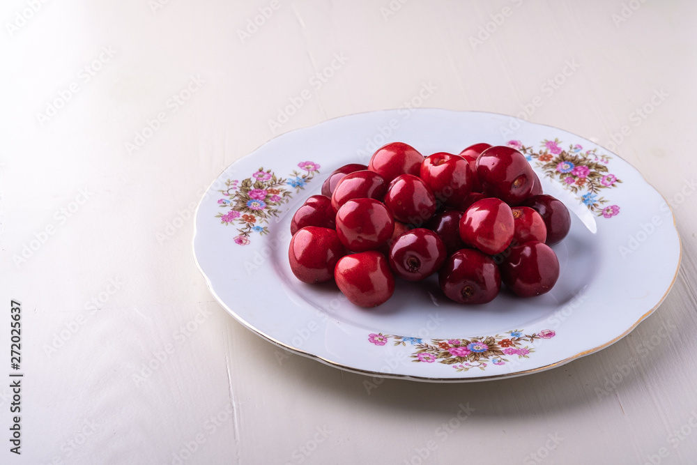 Cherry berries in white plate texture on wooden white background angle view Cherry berries in white plate texture on wooden white background angle view