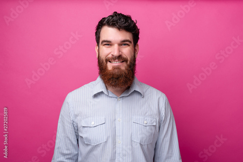 Portrait of smiling young bearded man in casual standing over pink background