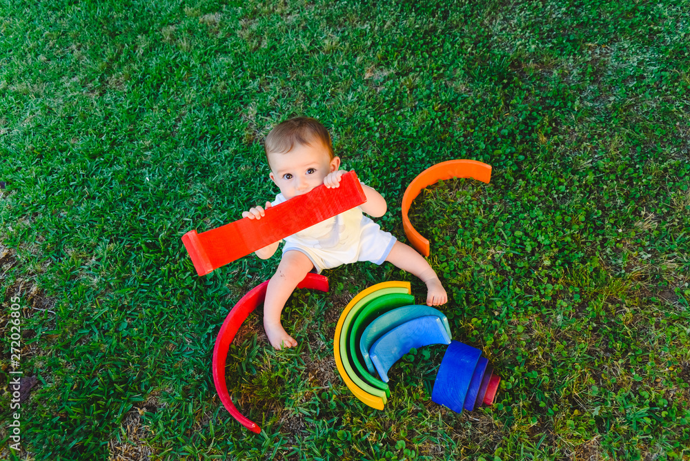 Baby playing with a colorful wooden rainbow on the grass, children's intellectual and mental development. Baby playing with a colorful wooden rainbow on the grass, children's intellectual and mental development.