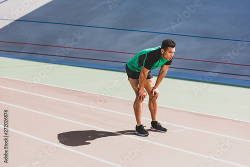 tired mixed race sportsman in sportswear standing at stadium with hands on knees