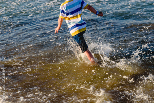 Young child having fun getting wet and splashing on the shore of the beach running between the waves.