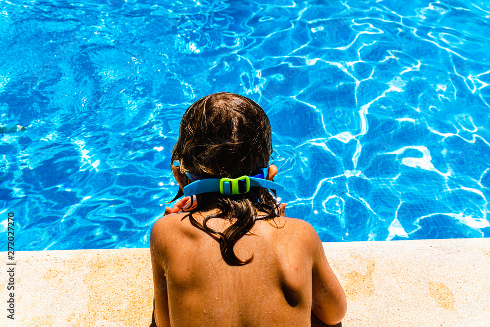 Φωτογραφία Child with a tanned back to the sun, observing the fresh and transparent water of a pool