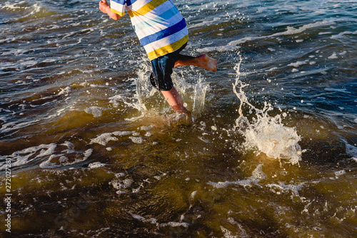 Fototapeta Naklejka Na Ścianę i Meble -  Child running on the sand of the beach splashing with waves in summer.