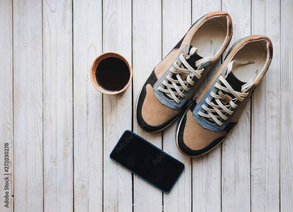 Modern suede new sneakers stand on a wooden white background and coffee. Sport, morning, movement, copy space, fees for work. A pair of trend shoes, phone and breakfast.