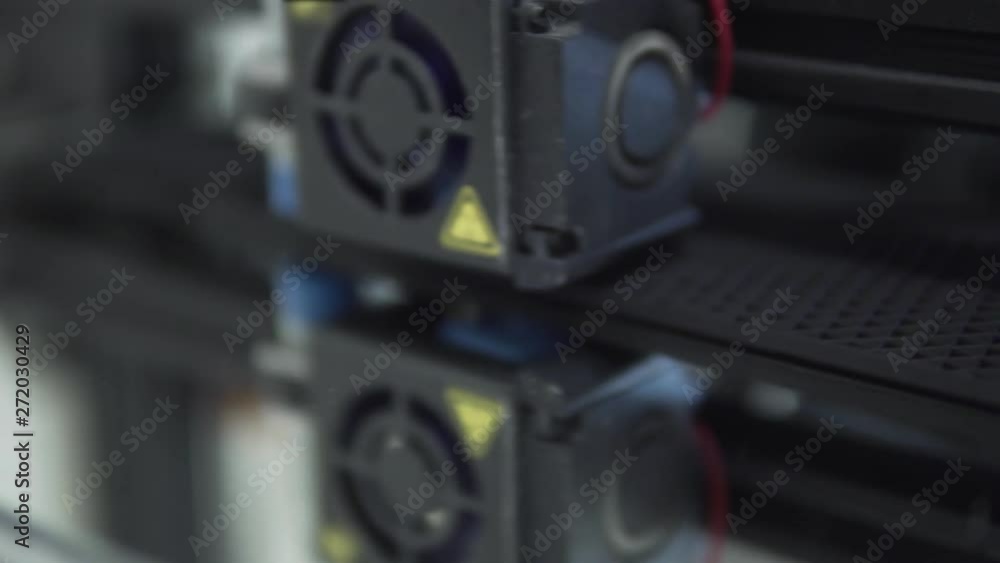Close up view to a FDM 3D Printer extruder while working on mirror glass with black PLA filament. Shallow depth of field. Close up view to a FDM 3D Printer extruder while working on mirror glass with black PLA filament. Shallow depth of field.