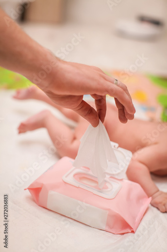 close up male hand pulls out a wet napkin. daily children's hygiene. paternity concept. newborn lying on his stomach in selective focus on the background