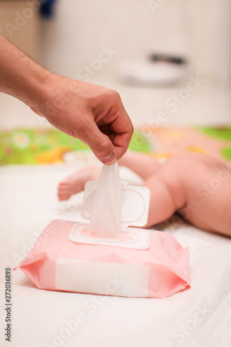 close up male hand pulls out a wet napkin. daily children's hygiene. paternity concept. newborn lying on his stomach in selective focus on the background photo