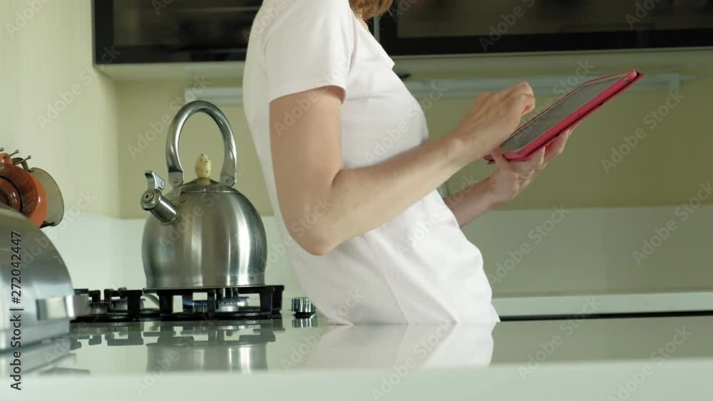 The woman in the kitchen uses the tablet, just woke up. Breakfast. Early morning The woman in the kitchen uses the tablet, just woke up. Breakfast. Early morning