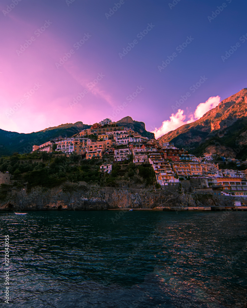Positano coast as seen from the water showing a pink sky and mountain looming in the background